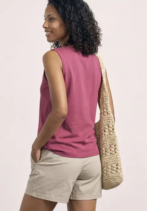 Achteraanzicht van een vrouw in een roze mouwloos shirt, beige short en gevlochten strotas op de schouder.