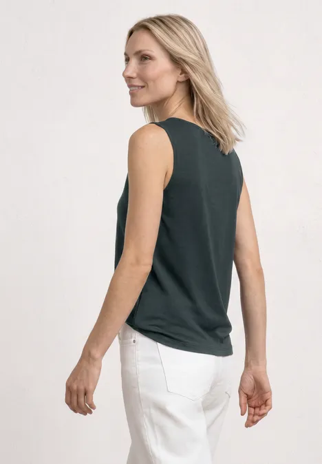 Vrouw van achteren in een zwarte mouwloze top en witte broek voor een lichte achtergrond.