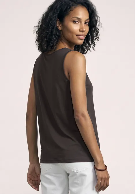 Vrouw met krullend haar van achteren, gekleed in een zwart mouwloos topje en witte broek.