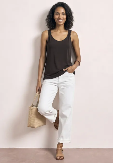 Vrouw in zwarte top en witte jeans met een strooien tas.