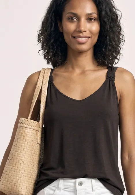 Vrouw met krullend haar draagt een zwart topje, lichte broek en gevlochten strooien tas; gezicht onscherp.