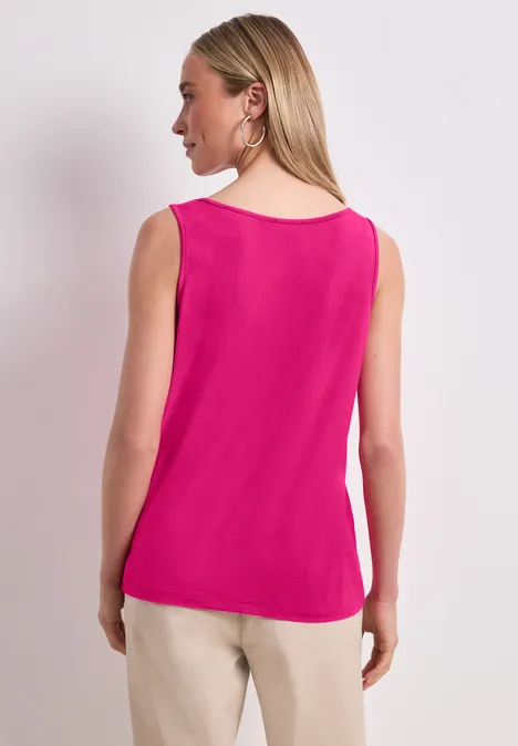Achteraanzicht van een vrouw in een fuchsia mouwloze top en beige broek voor een neutrale achtergrond.