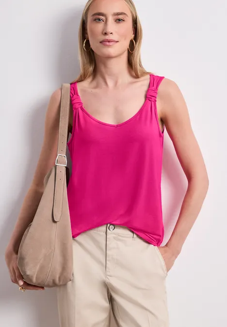 Vrouw in roze top, beige broek en een bijpassende beige schoudertas.