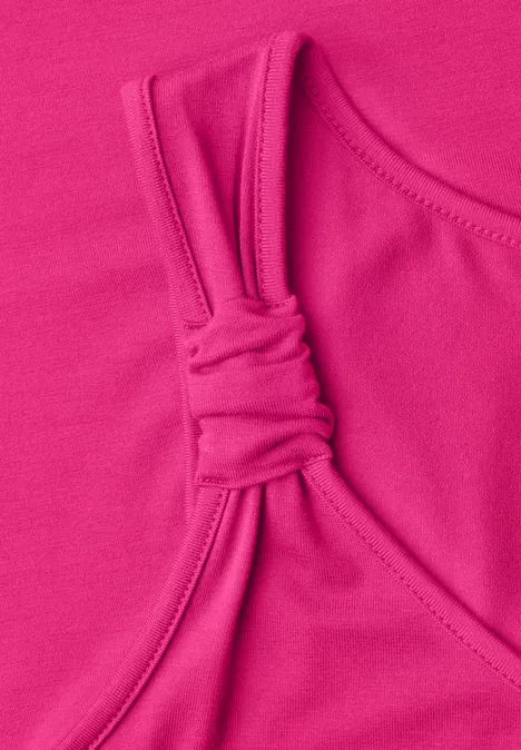 Close-up van een felroze top met een knoopdetail aan het bandje