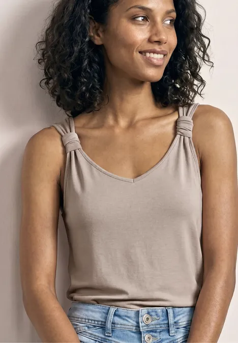 Top mit V-Neck und Knotendetail clay sand Beige ärmelloses Top mit eingedrehten Trägern, blaue Jeans, Person vor neutralem Hintergrund.