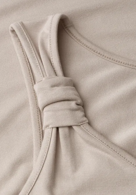 Top mit V-Neck und Knotendetail clay sand Nahaufnahme eines beigen Baumwollstoffs mit geknotetem Träger an einem Oberteil.