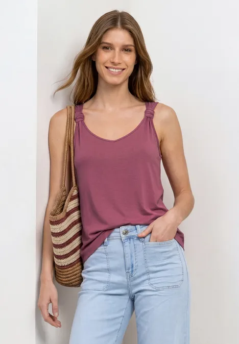 Top mit V-Neck und Knotendetail dark clouded blush Frau in ärmellosem, rostfarbenem Top und Jeans, mit geflochtener Basttasche über der Schulter.