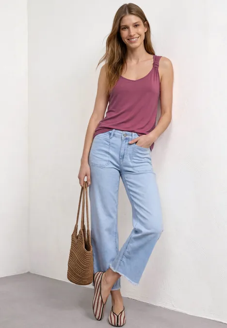 Top mit V-Neck und Knotendetail dark clouded blush Frau in lässigem Look: lila Top, helle Jeans, Sandalen und Korbtasche vor weißer Wand.