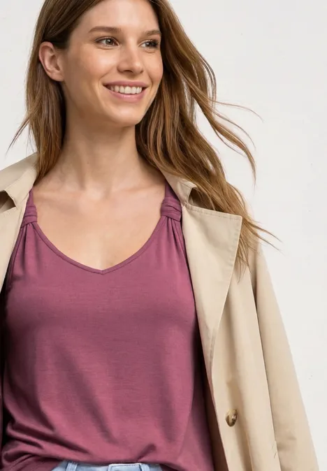 Top mit V-Neck und Knotendetail dark clouded blush Frau in einem rosafarbenen ärmellosen Top und einem hellbeigen Mantel.