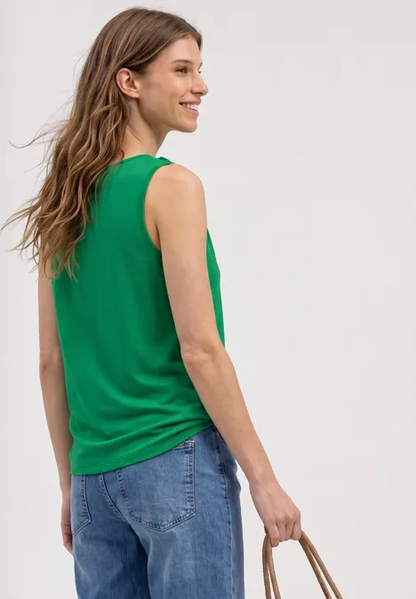 Persoon van achteren in een groen mouwloos topje en blauwe jeans, met een gevlochten stromand.