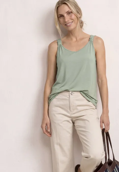 Top mit V-Neck und Knotendetail mint leaf Frau in lockerem grünen Top und beigen Jeans hält eine braune Tasche vor hellem Hintergrund.