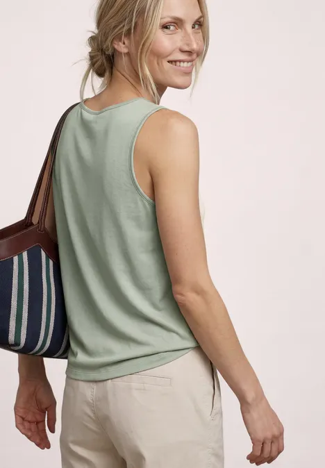 Top mit V-Neck und Knotendetail mint leaf Frau von hinten in grünem Tanktop, beiger Hose und gestreifter Handtasche.