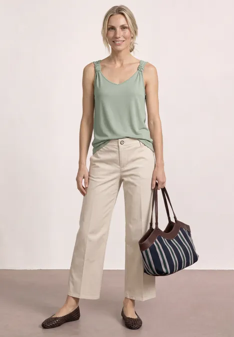 Top mit V-Neck und Knotendetail mint leaf Eine Frau in grünem Top und beigen Hosen, trägt eine gestreifte Tasche und braune Schuhe.