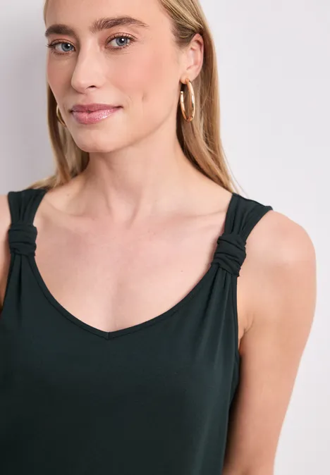 Close-up van vrouw in zwart hemdje met geknoopte bandjes, lichte huid en gouden creolen.