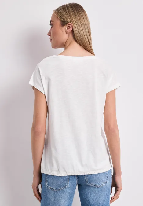 Frau von hinten in weißem T-Shirt und blauen Jeans vor hellem Hintergrund.