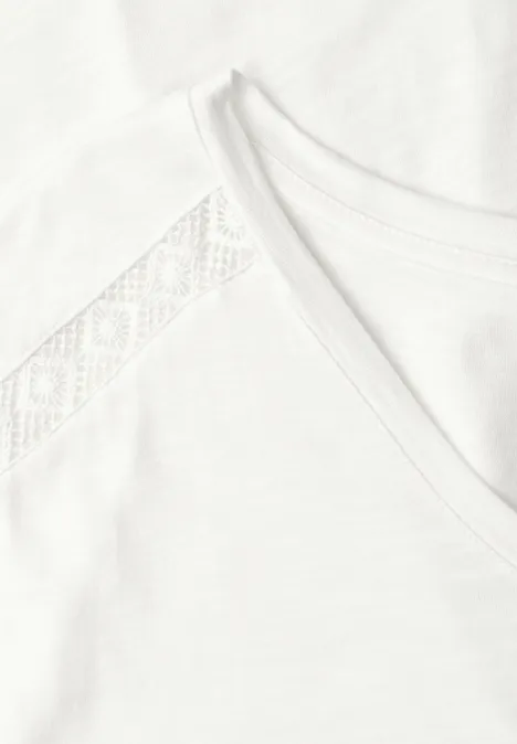 Nahaufnahme eines weißen T-Shirts mit Spitzenbesatz an der Schulter und Rundhalsausschnitt.