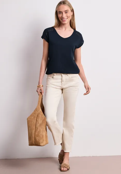 Frau trägt schwarz T-Shirt, helle Jeans, Keilabsatz-Sandalen und große Wildleder-Tasche.