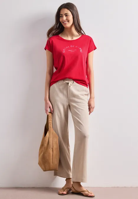 Dropped Shoulder Shirt mit Rundhals salsa red Frau in rotem T-Shirt, beiger weiter Hose, Sandalen und großer brauner Tasche.