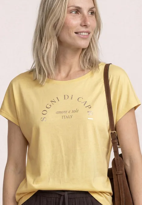 Koszulka na ramiączkach z okrągłym dekoltem soft yellow Uśmiechnięta blondynka w żółtej koszulce z napisem, z torbą na ramię.