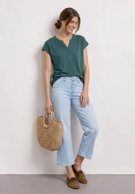 Dropped Shoulder Shirt mit Split Neck mediterra green Person trägt grüne Bluse, hellblaue Jeans und braune Schuhe und hält eine geflochtene Korbtasche vor weißer Wand