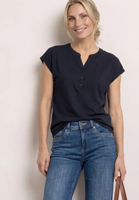 Dropped Shoulder Shirt mit Split Neck shadowed navy Frau in dunkelblauer Bluse und Jeans steht vor hellem Hintergrund und hält eine Tasche in der Hand.