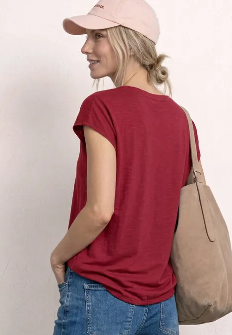 Dropped Shoulder Shirt mit Split Neck truffle red Frau von hinten in rotem T-Shirt, Jeans, rosafarbener Cap und beiger Tasche.