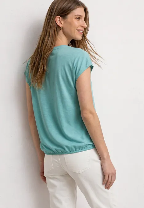 Dropped Shoulder Shirt mit Split Neck misty mint Eine Frau ist von hinten in einem grünen T-Shirt und weißen Hosen zu sehen.