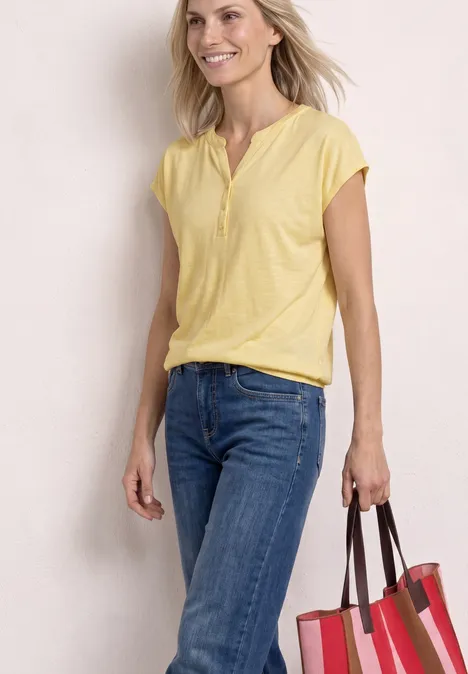 Een vrouw in geel shirt en jeans draagt een grote rode tas.