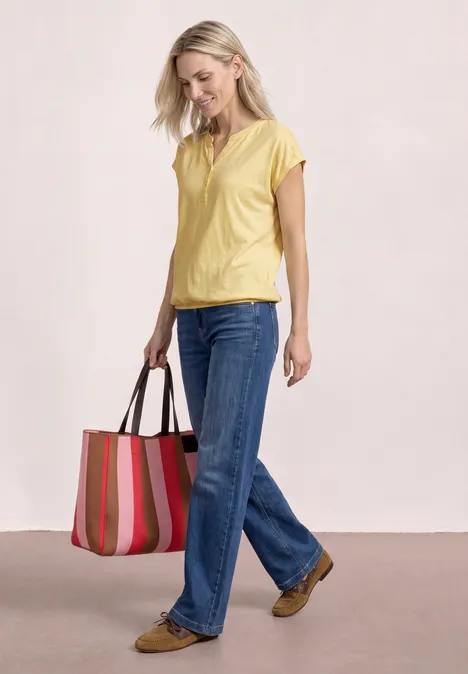 Vrouw in geel shirt en blauwe jeans met een kleurrijke strepenhandtas.