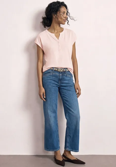 Dropped Shoulder Shirt mit Split Neck minimal rose Frau in hellem kurzärmeligen Shirt, weiter blauer Jeanshose mit Gürtel und braunen Loafers