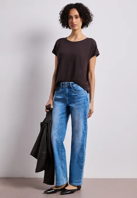 Shirt met boothals en schouderdetails espresso brown Persoon staat in wijde spijkerbroek, donker T-shirt en houdt een zwarte jas vast.