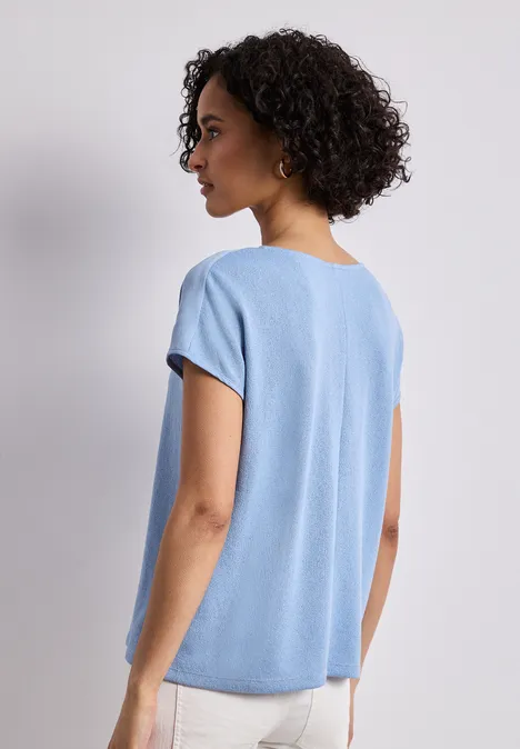 Frau von hinten in locker sitzendem hellblauen T-Shirt, kurze lockige Haare