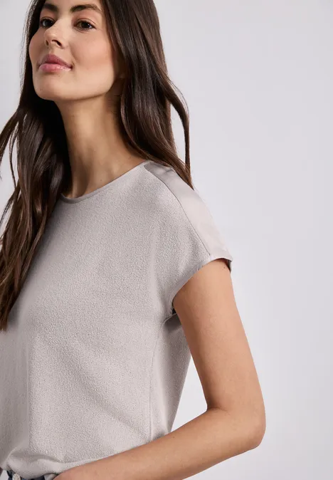 Frau im cremefarbenen, locker sitzenden T-Shirt mit kurzen Ärmeln vor neutralem Hintergrund.