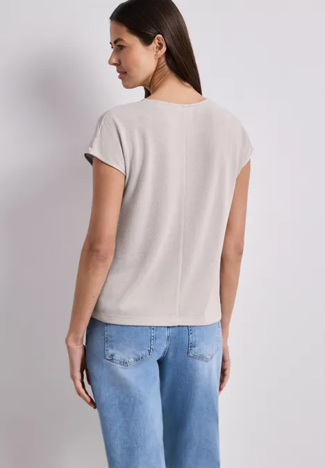 Frau steht mit dem Rücken zur Kamera, trägt beiges T-Shirt und blaue Jeans.