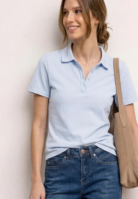 Kurzarm Poloshirt in Rippstruktur cashmere blue Frau in hellblauem Poloshirt und Jeans, lächelt und trägt eine beige Umhängetasche.
