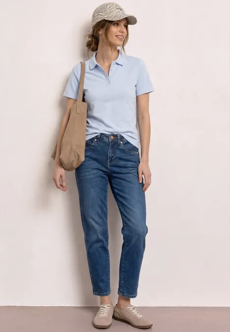 Kurzarm Poloshirt in Rippstruktur cashmere blue Frau steht vor hellem Hintergrund, trägt hellblaues Poloshirt, blaue Jeans, Sneakers und große Beuteltasche.