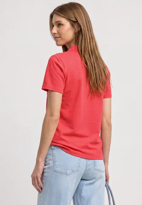 Femme de dos portant un t-shirt rouge et un jean clair, tenant un sac à main.
