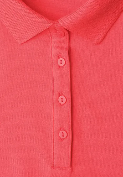 Gros plan d’un polo corail avec col et quatre boutons.