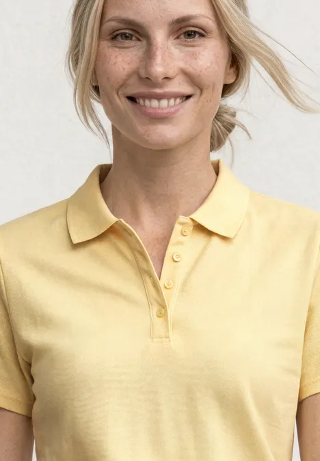 Eine Frau trägt ein hellgelbes Poloshirt, ihr Gesicht ist unscharf.