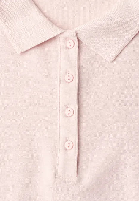 Close-up van een pastelroze poloshirt met kraag en vier knopen.