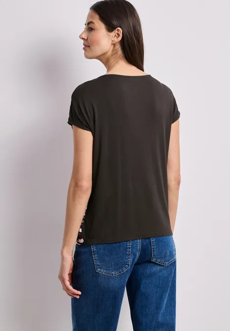 Frau von hinten in schwarzem T-Shirt und blauen Jeans vor hellem Hintergrund.