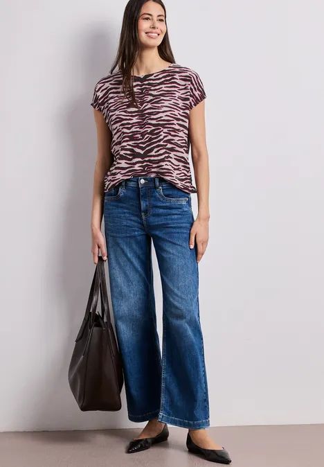 Frau trägt kurzärmeliges Zebramuster-T-Shirt, weite Jeans, schwarze Ballerinas und große schwarze Tasche.