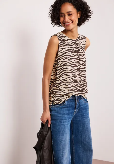 Vrouw draagt een zebraprint top, wijde jeans en houdt een zwarte tas vast.