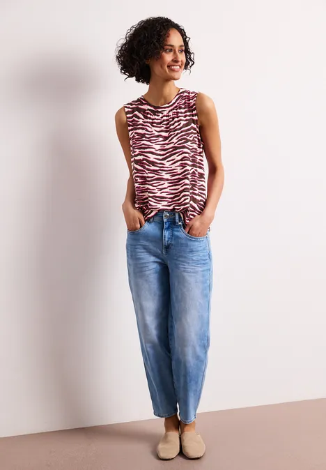 Person in rot-weiß gestreiftem Top, blauen Jeans und beigen Schuhen steht entspannt mit Händen in den Taschen.