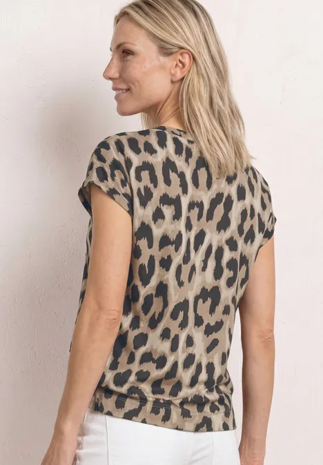 Vrouw van achteren in een beige luipaardprint top en witte broek tegen een lichte achtergrond.