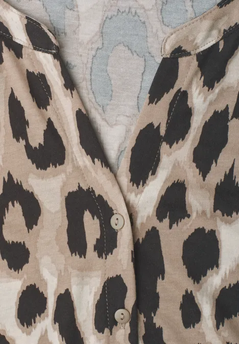 Close-up van een beige kledingstuk met zwart luipaardpatroon en zichtbare knopen.