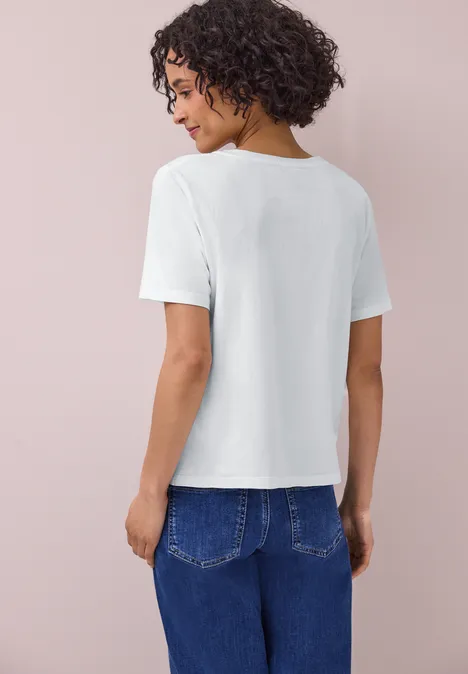 Eine Frau von hinten, in weißem T-Shirt und blauen Jeans vor pastellrosa Hintergrund.