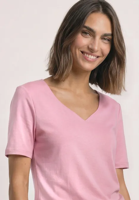 Kurzarm Shirt mit Herzausschnitt vintage blush Eine lächelnde Frau trägt ein rosa T-Shirt mit V-Ausschnitt vor hellem Hintergrund.