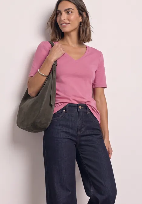 T-shirt manches courtes à col cœur warm blush Frau trägt rosa T-Shirt, dunkelblaue Jeans und hält eine olivgrüne Tasche.