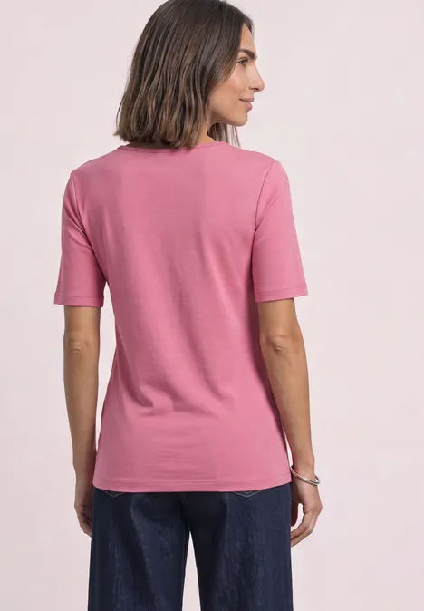 T-shirt manches courtes à col cœur warm blush Frau von hinten in rosa T-Shirt und blauen Jeans, Arme locker an den Seiten.